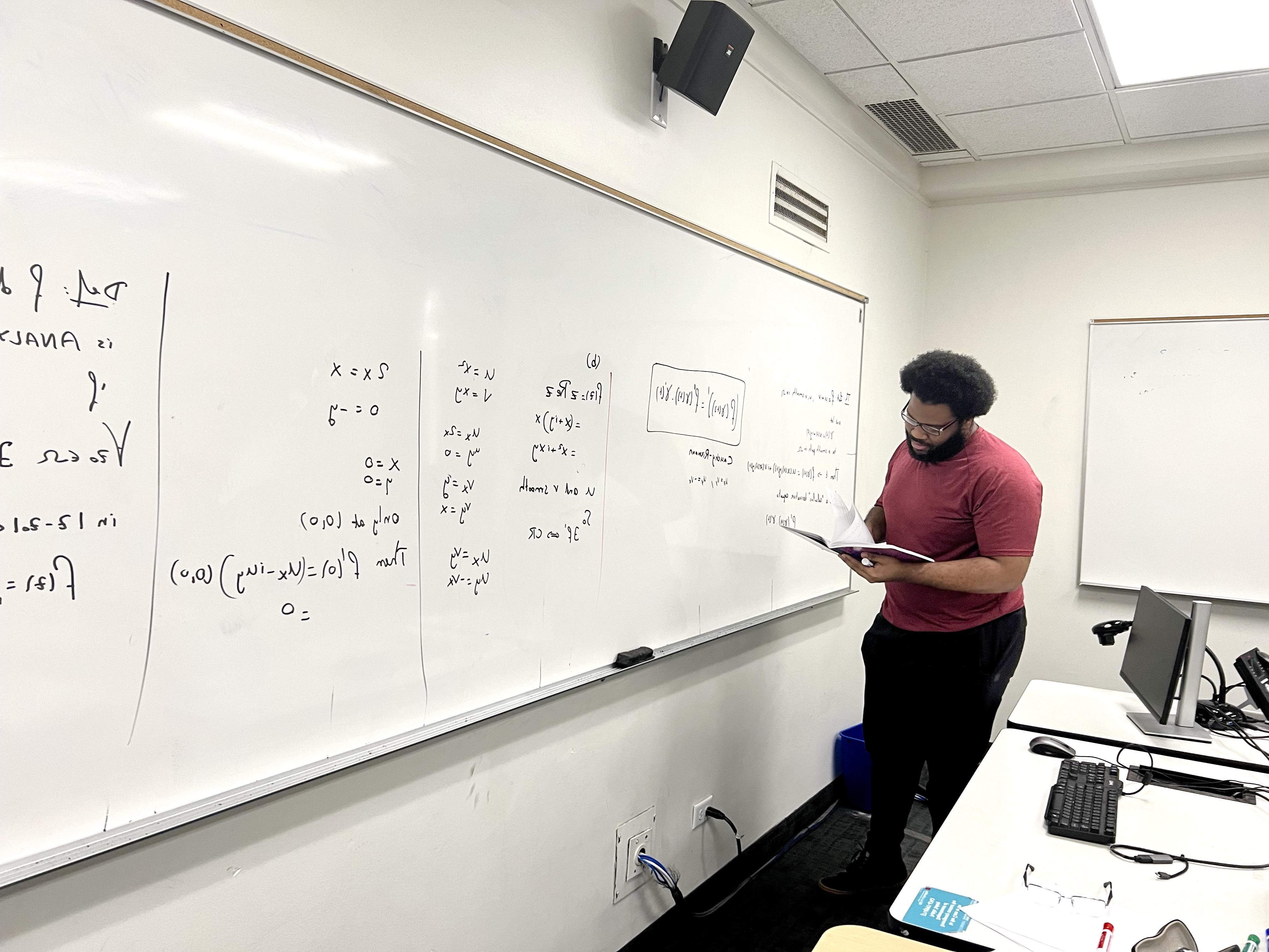 Student with textbook writing at whiteboard.